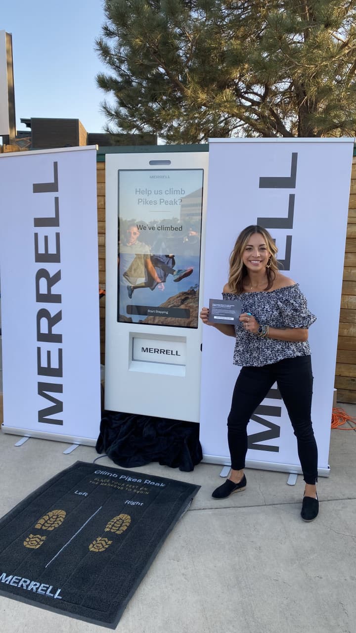 Winner with prize card next to full Merrell kiosk setup with branded banners